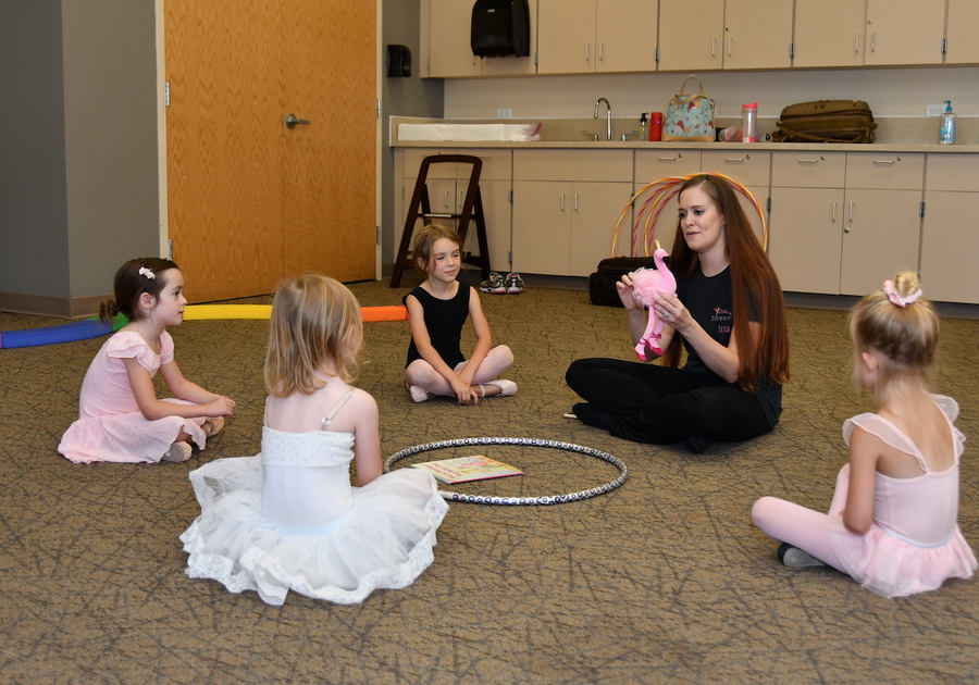 4 young ballerinas sitting cross-legged on the floor with their dance instructor
