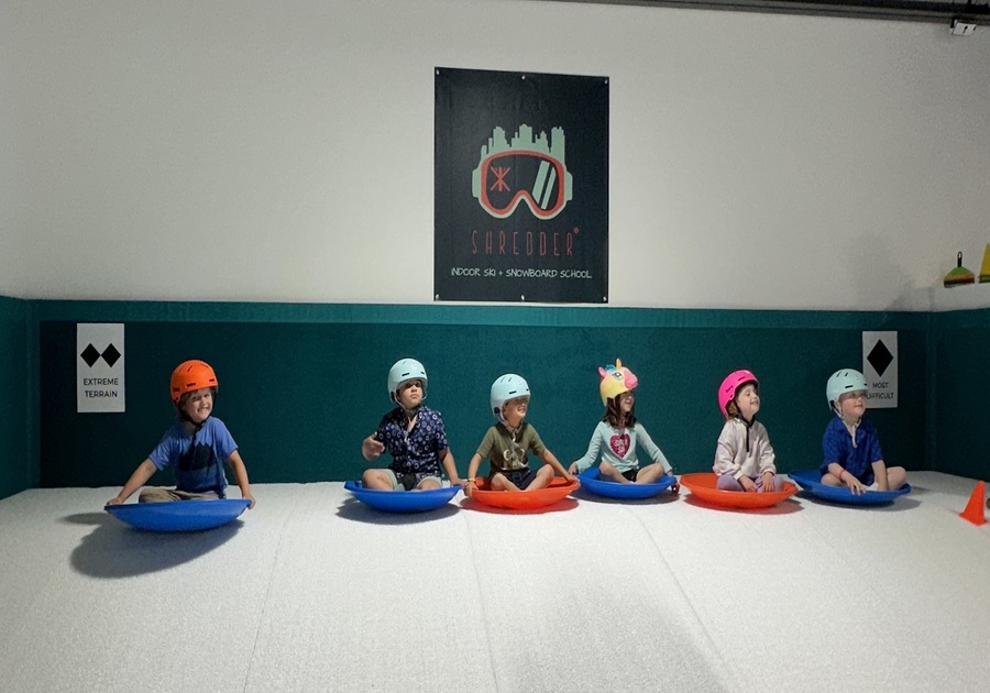 group of kids wearing helmets sledding down indoor hill