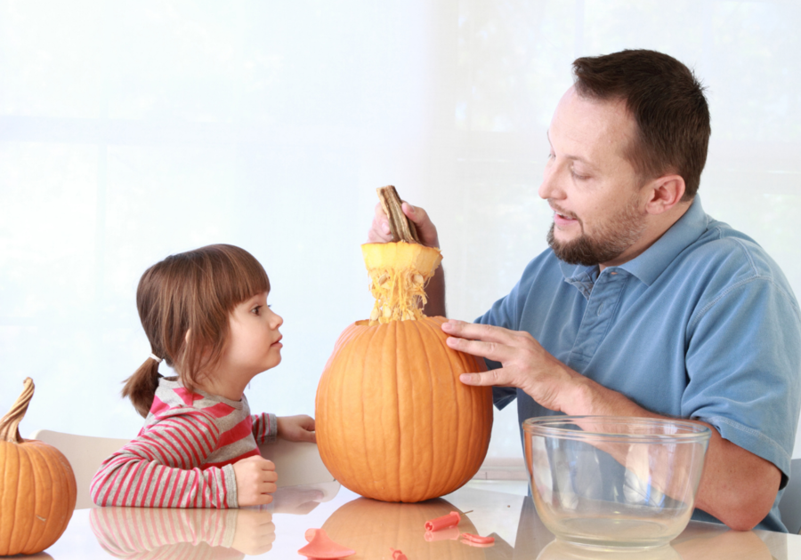 dad pulling off pumpkin top in front of little girl