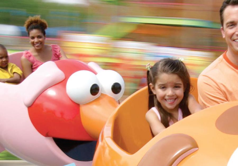A father and daughter smile on the spinning Elmo ride, Mother and child smile in the background on the same ride