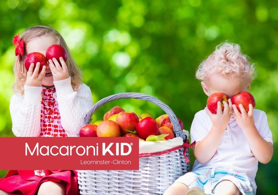 Two young children holding apples up to theirs eyes and laughing in an apple orchard