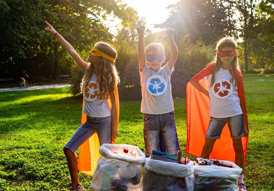 Kids dressed like super heroes standing behind recycling bags. They are expressing excitement about recycling.