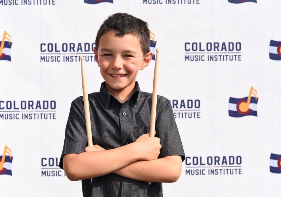 child holding drumsticks in front of Colorado Music Institute banner