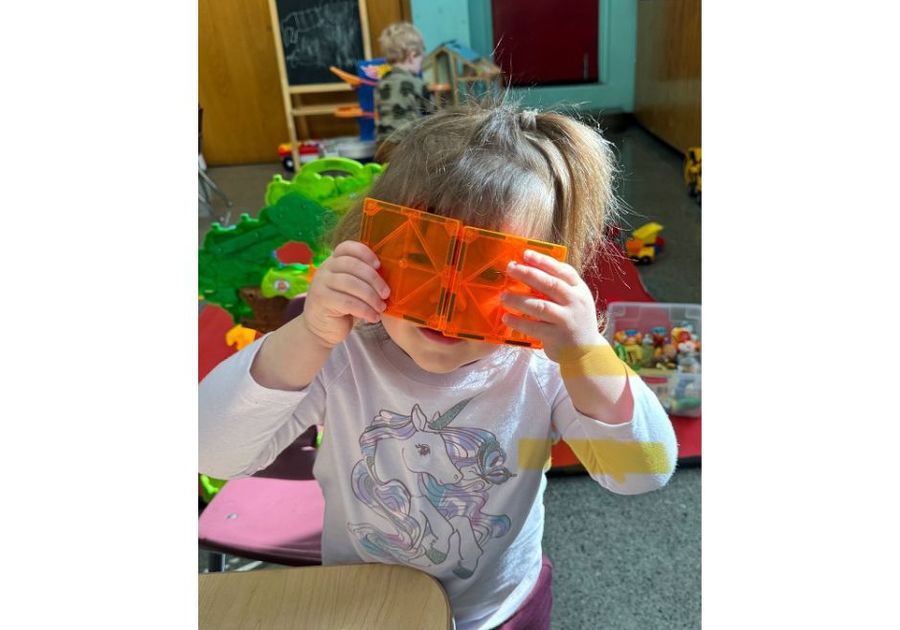 toddler looking through two orange magnatiles