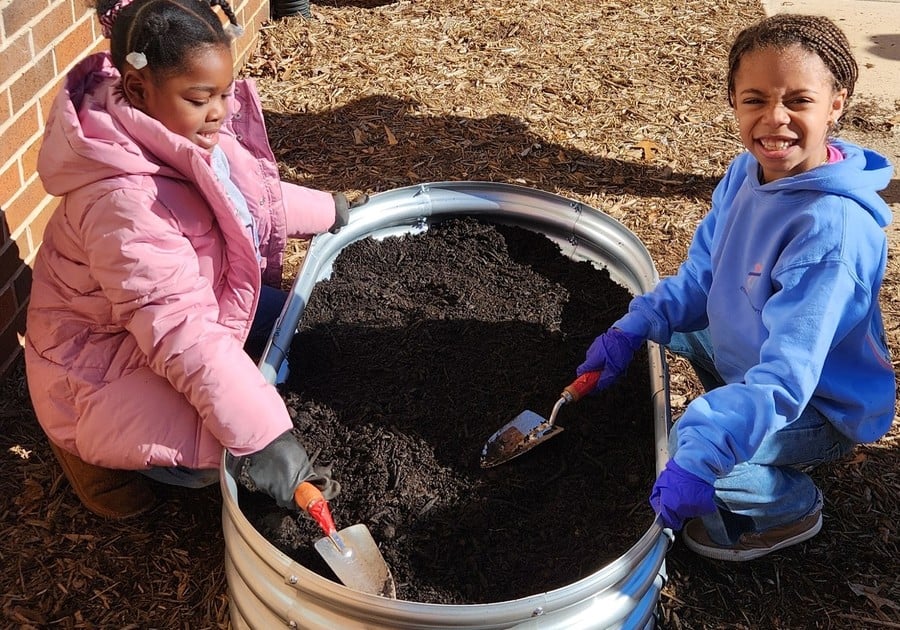 photo of two female children digging in garden dirt outside