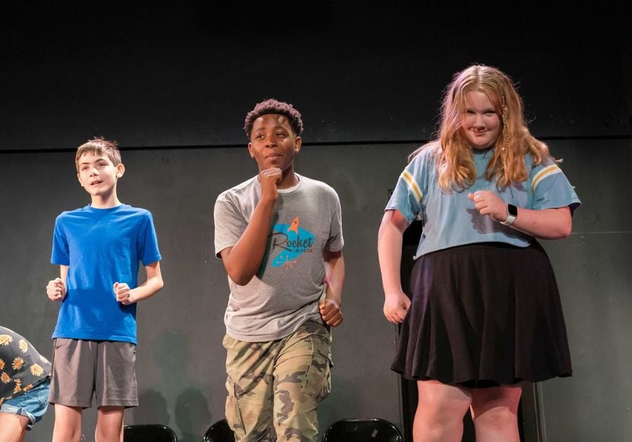 Three kids on a theater stage doing improv