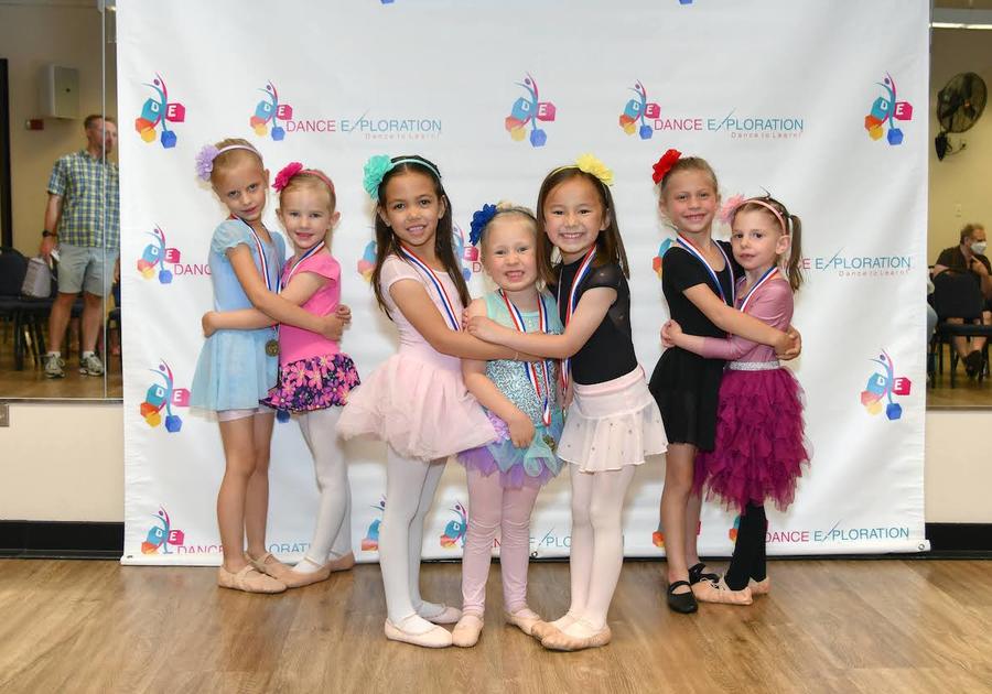 7 young ballerinas posing for a picture in front of a Dance Exploration backdrop