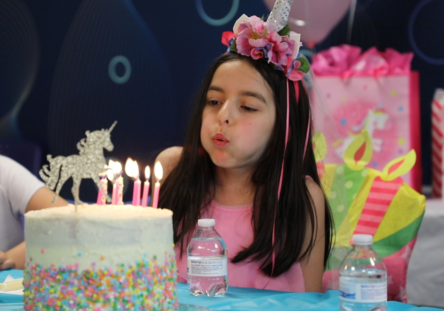 girl blowing out birthday candles on a unicorn cake
