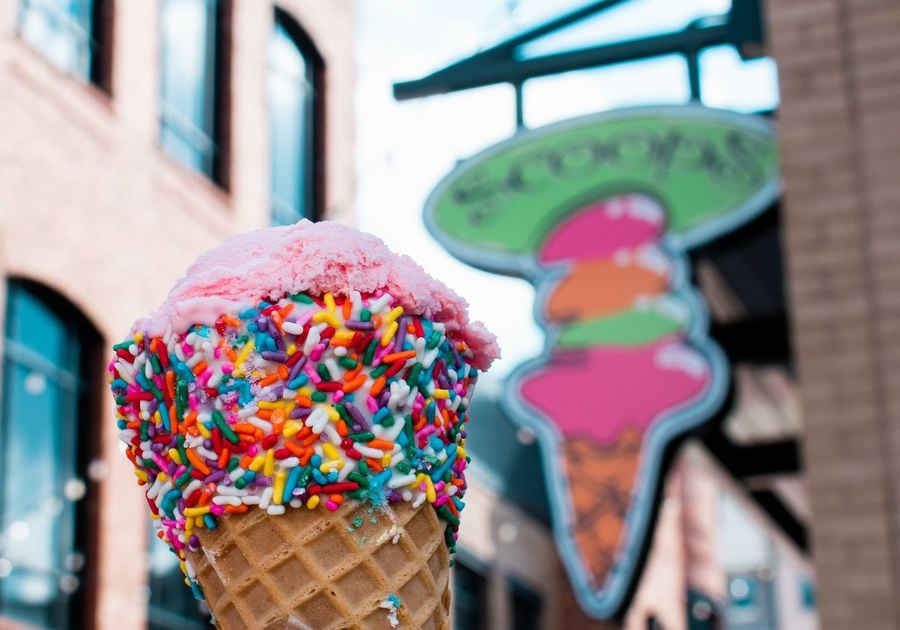 Hand holding ice cream cone with sprinkles in front of Scoops sign