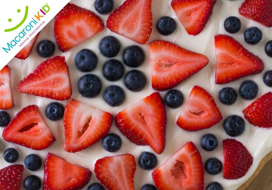 A picture of a large sugar cookie covered with cream cheese and fruit.