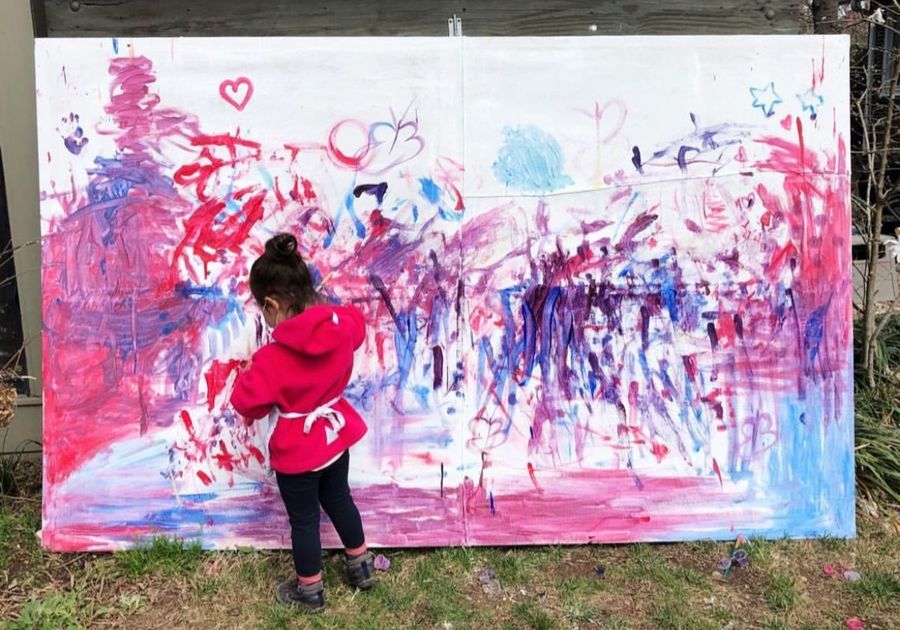 Child standing in front of large paint canvas outdoors