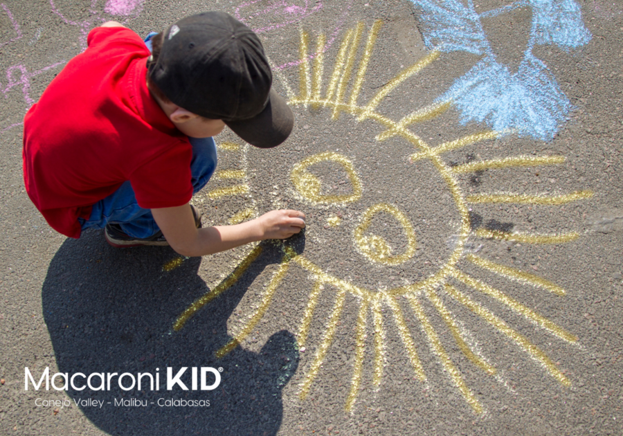 Young boy drawing a happy face sun with sidewalk chalk