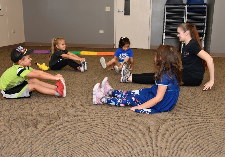 3 girls and a boy with their dance teacher, sitting on the floor and stretching their legs