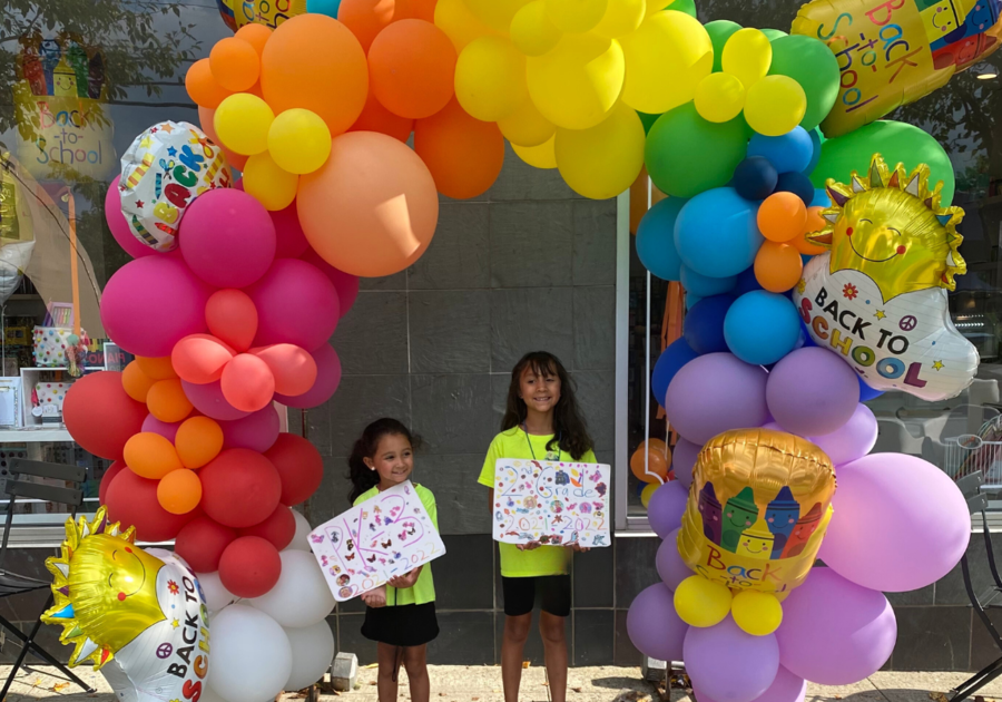 2 girls in front of a back to school balloon arch