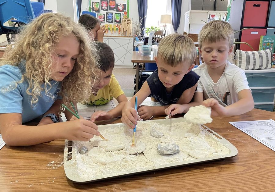 Four children with paintbrushes and sand