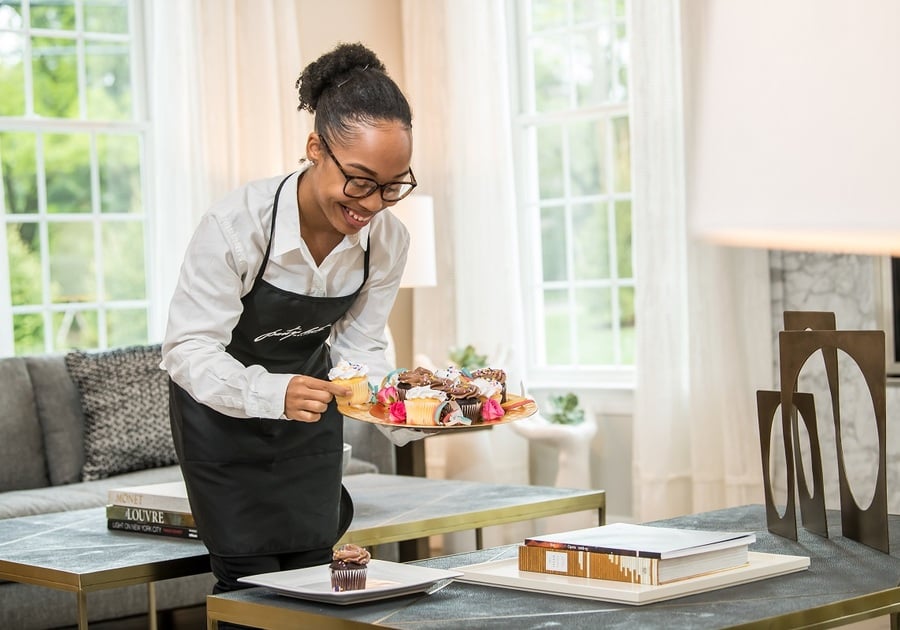 woman in apron arranging cupcakes on plate