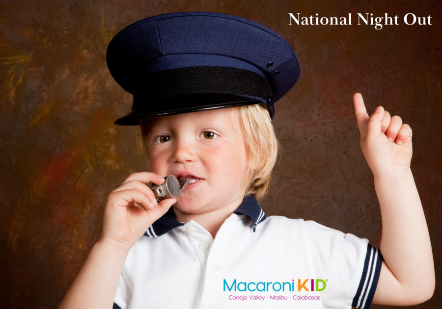 National Night Out, little boy wearing a police hat, blowing a metal whistle and pointing up to National Night Out