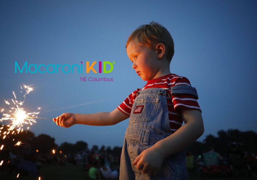 young boy holds a lit sparkler against a dark blue sky