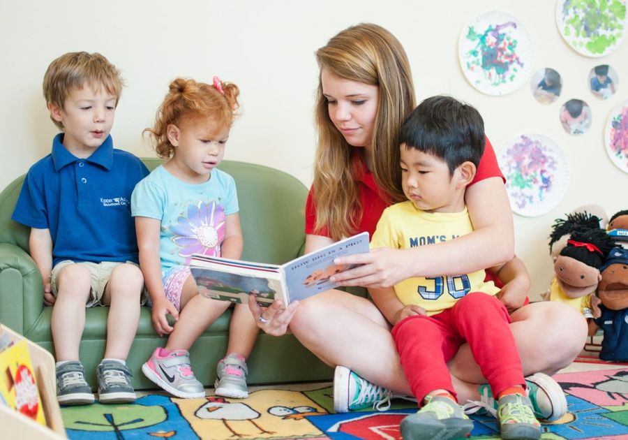 preschool teacher with boy in lap reading to three kids
