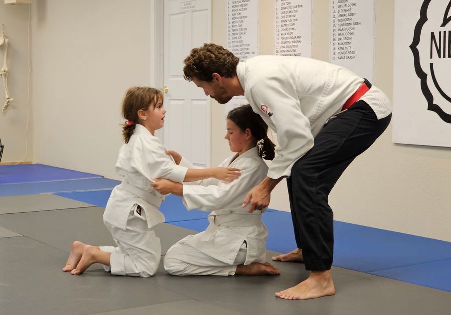 2 girls kneeling, learning jujisu from their instructor