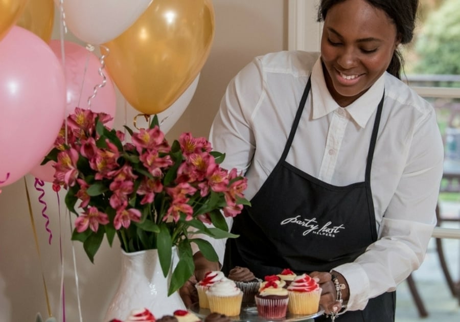 women in apron arranging cupcakes on party table