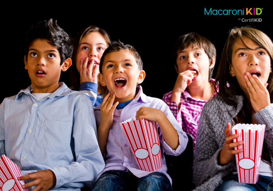 Kids watching a scary movie with bowls of popcorn. Some are laughing and some look scared.