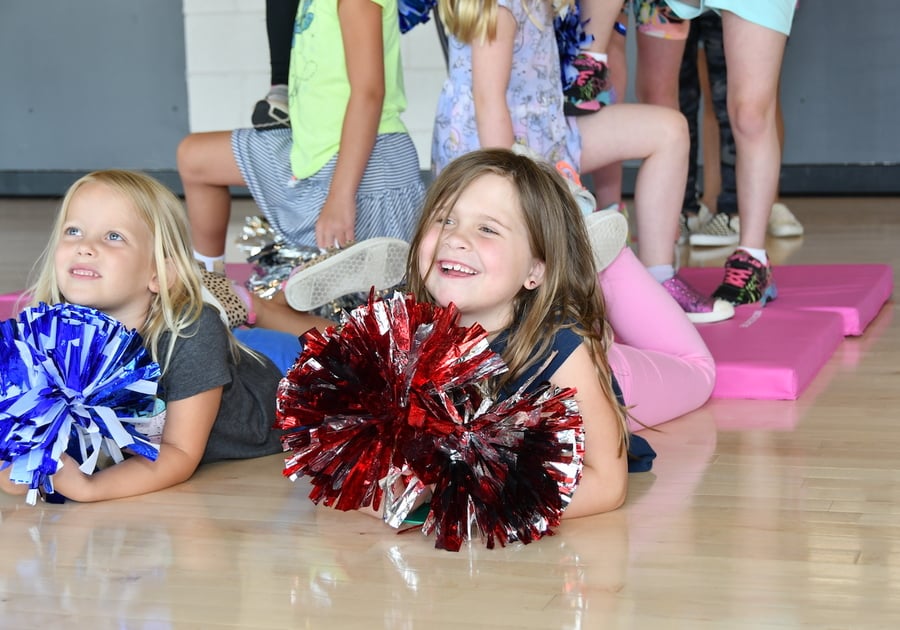 2 young smiling girls lying in their stomachs and holding cheer pompoms