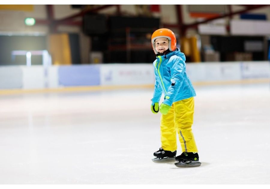 A single young child ice skating wearing a helmet
