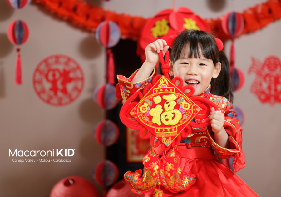 Little girl with a big smile holding up red decorations for Chinese New Year