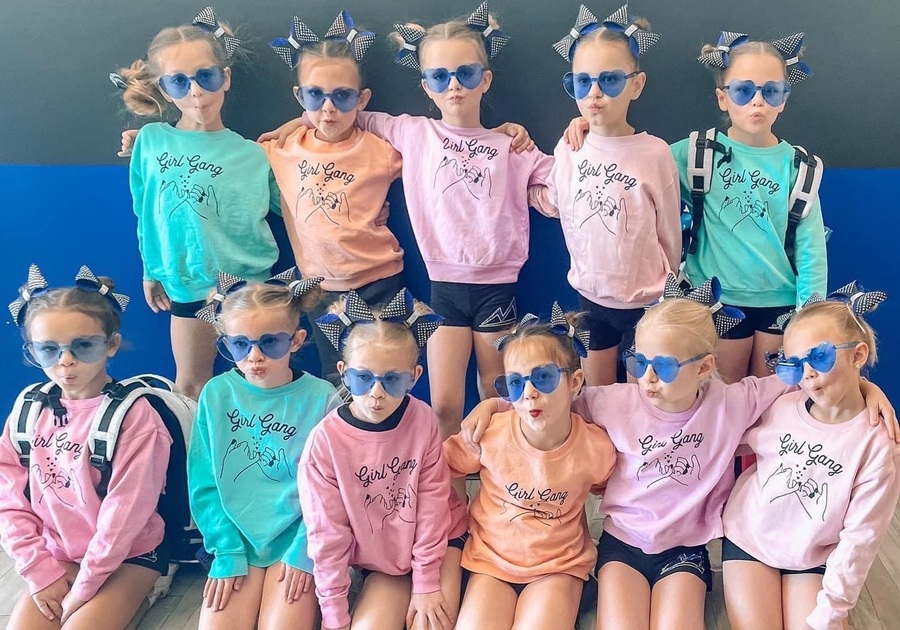 11 young girls wearing matching sunglasses, hair ribbons, and sweatshirts that say Girl Gang