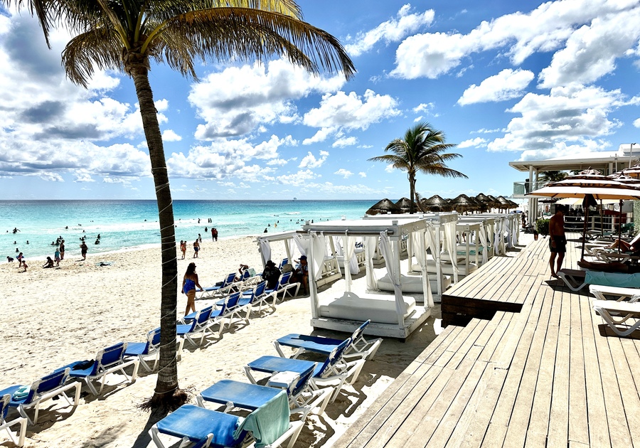 A gorgeous beach in Cancun, located at the Wyndham Alltra Resort. Photo depicts blue skies, palm trees and beach cabanas along a turquoise Caribbean Sea