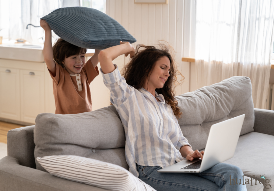 mom trying to work on a laptop while her kid hits her with a pillow