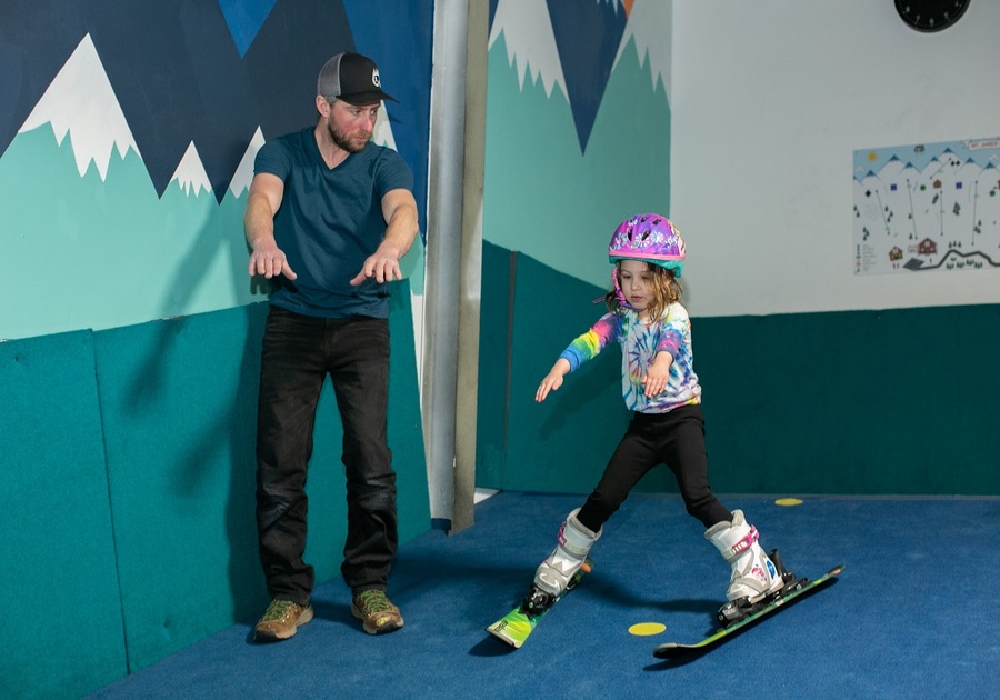 instructor teaching kid how to ski indoors