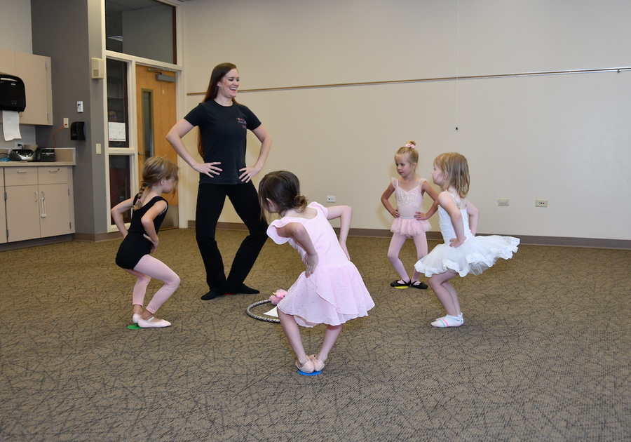 4 young ballerinas standing in a circle with their dance teacher learning to plie