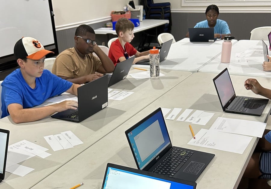 photo of children seated at table using laptops