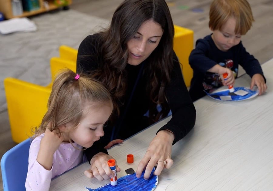 teacher helping preschooler with gluestick