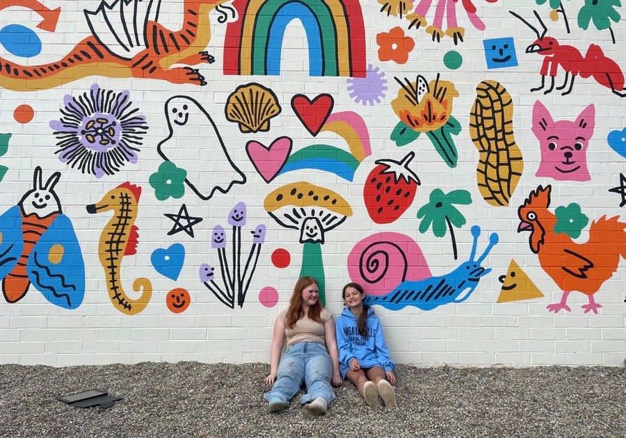 2 females sitting against decorated wall