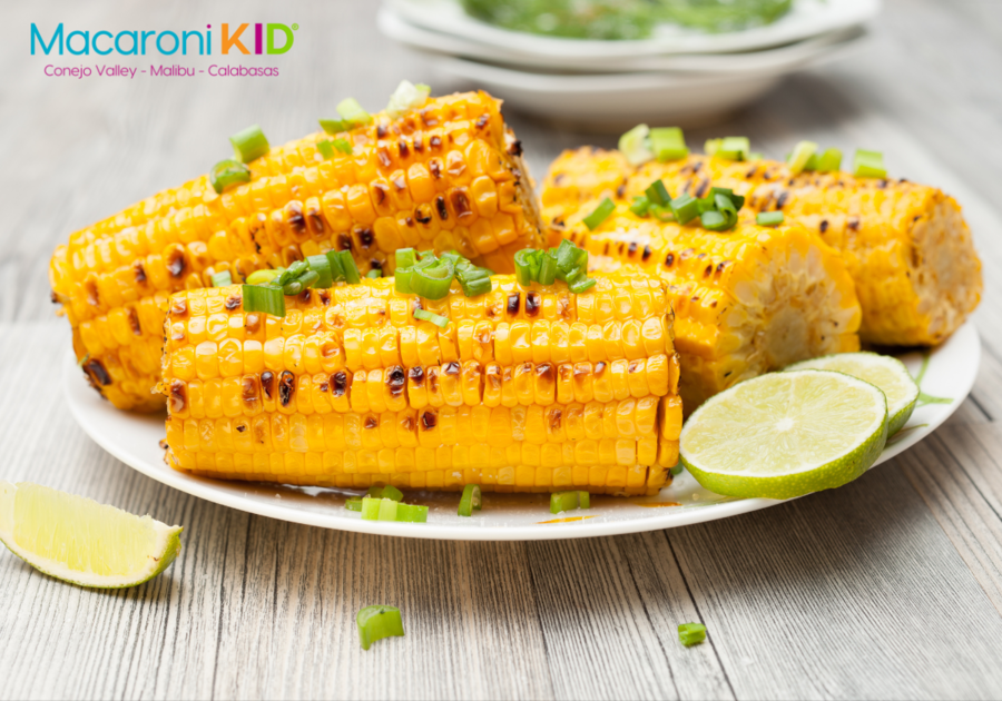BBQ corn on the cob on a plate with green onions and limes