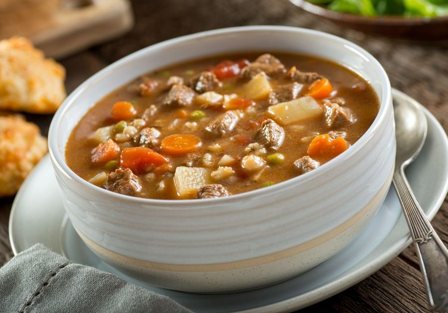 A cozy white ceramic bowl filled with hearty beef stew, complemented by a side of vibrant salad and golden-brown biscuits