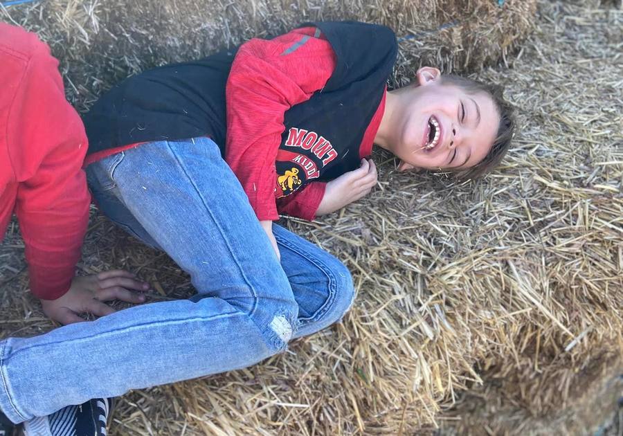 A child laughs while tumbling in hay at Paulus Farm Market in Mechanicsburg, PA—where farm fun meets childhood magic!