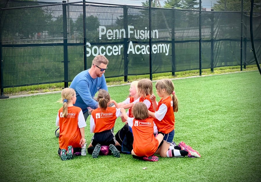 Penn Fusion coahc and soccer players kneeling in a huddle on the field