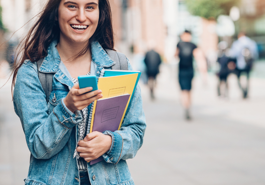 college student looking at camera with books and cell phone