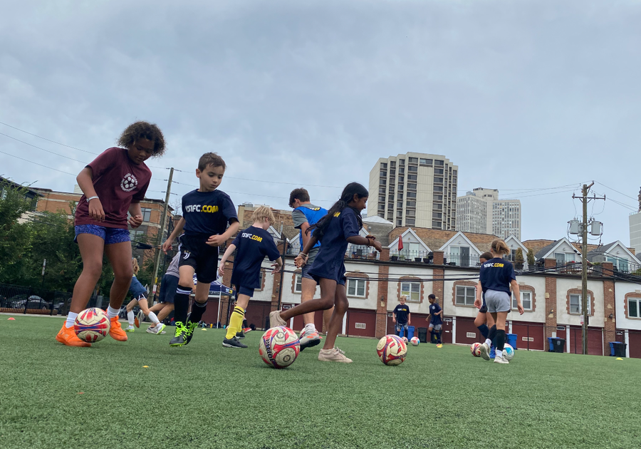 kids dribbling soccer balls on field