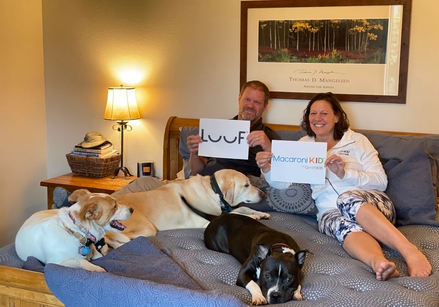 Parents and dogs lounging on Luuf Mattress holding Luuf and Macaroni KID signs