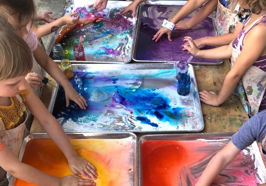 female campers getting hands into pans of paint