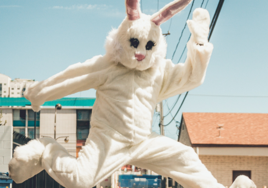 Person dressed as Easter Bunny jumping in air with buildings behind