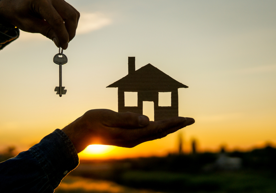 Sunset city in background, hand holding house cutout and hand holding key