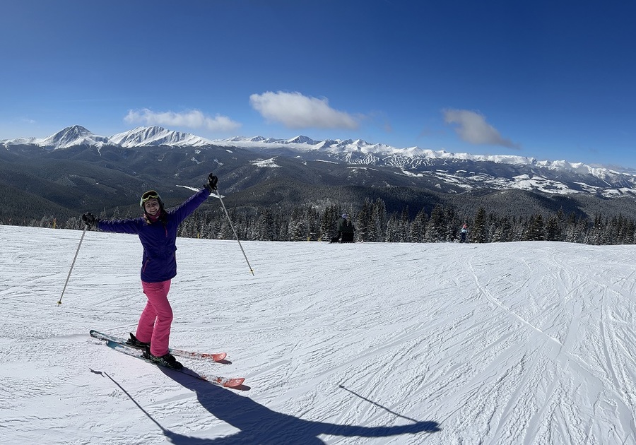 girl skiier at mountain summit with snow capped mountains in background