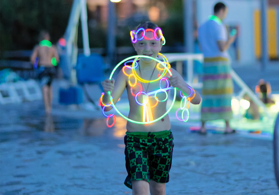 Boy in swim trunks near swimming pool at dusk wearing lots of glow in the dark necklaces