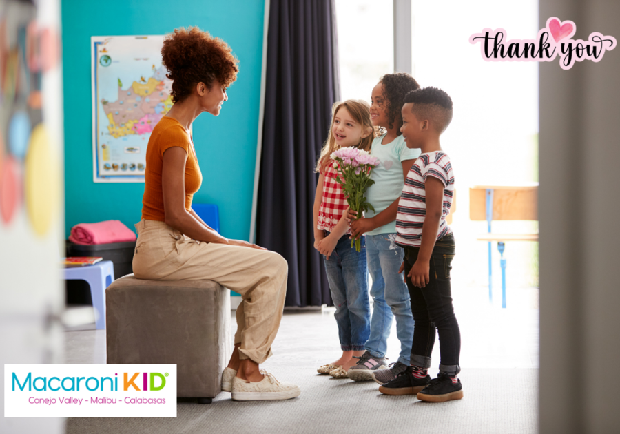 Three young kids standing in front of a teacher holding flowers